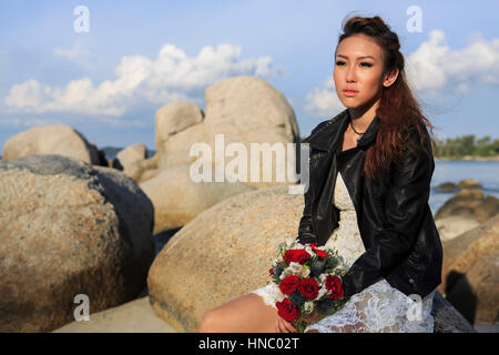 La donna in un abito da sposa seduto sulla spiaggia Foto Stock