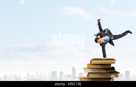 Giovane imprenditore allegro facendo handstand sulla pila di libri Foto Stock