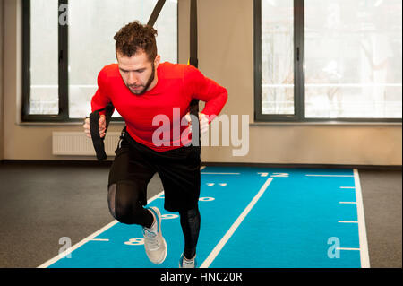 Ricci bianco barbuto uomo sportivo esercitando con cinghie di fitness in palestra Foto Stock