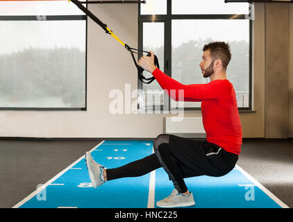 Ricci bianco barbuto uomo sportivo esercitando con cinghie di fitness in palestra Foto Stock