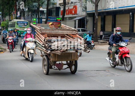 A Saigon, Vietnam, Nov 2016 - Uomo offrendo una grande quantità di ponteggio usando un sovraccarico di scooter a tre ruote su una strada trafficata in Ho Chi Foto Stock