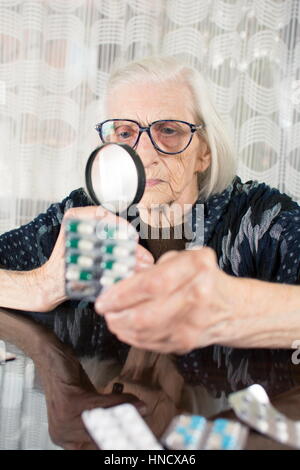 La nonna con lente di ingrandimento per determinare il nome del medicinale Foto Stock