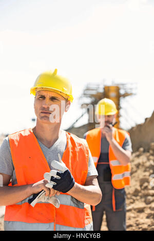 Lavoratore di sesso maschile permanente al sito di costruzione con il collega in background Foto Stock