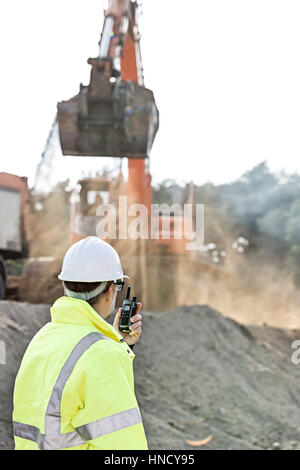 Vista laterale dell'ingegnere utilizzando un walkie-talkie al sito in costruzione Foto Stock