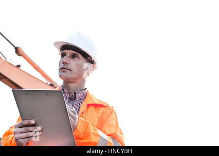 Il supervisore che guarda lontano mentre si tiene negli appunti contro il cielo chiaro Foto Stock