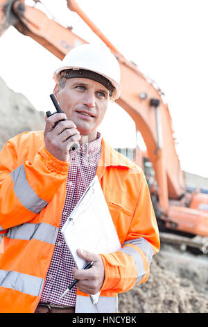 Supervisore negli appunti di trattenimento durante l'uso di walkie-talkie al sito in costruzione Foto Stock