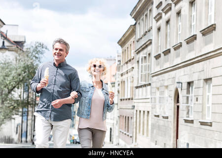 Felice di mezza età giovane azienda coni gelato mentre passeggiate in città Foto Stock