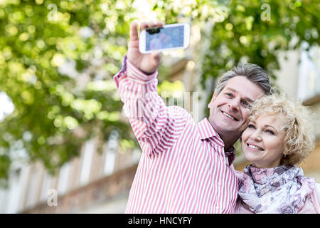 Felice di mezza età giovane tenendo selfie attraverso il telefono cellulare all'aperto Foto Stock