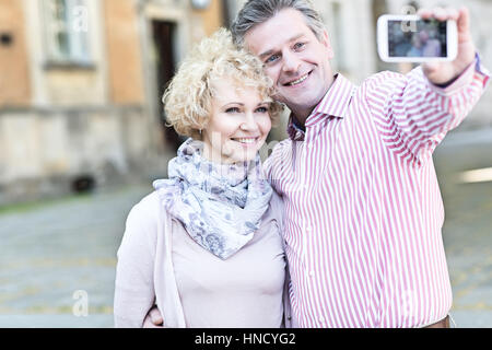 Felice di mezza età giovane tenendo selfie attraverso smart phone in città Foto Stock