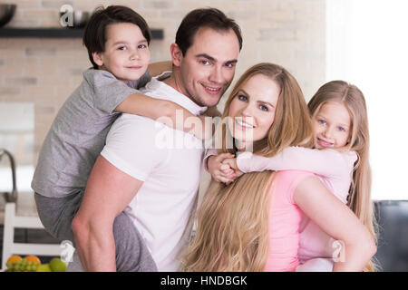 Ritratto di famiglia felice, padre e madre dando un ragazzo e una ragazza piggy back ride a casa Foto Stock