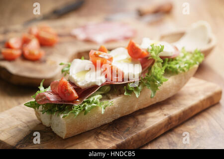 Aprire il panino con prosciutto, mozzarella e pomodori sul tavolo da cucina, fondale focus Foto Stock