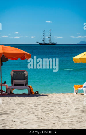 Sedie a sdraio con ombrelloni colorati con un tall ship in distanza, Philipsburg, Saint Maarten Foto Stock