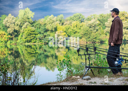 Le avventure di pesca. Fisherman e carp fishing ingranaggio. Fisherman vicino al carpfishing attrezzature sulle rive di un fiume in una giornata di sole Foto Stock