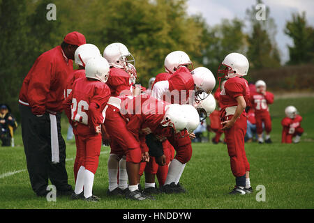 I bambini piccoli su una squadra di football americano in un huddle con il quarterback dando istruzione Foto Stock