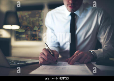 Imprenditore serio firma contratto in ufficio, lavorando di notte le ore di lavoro straordinario Foto Stock