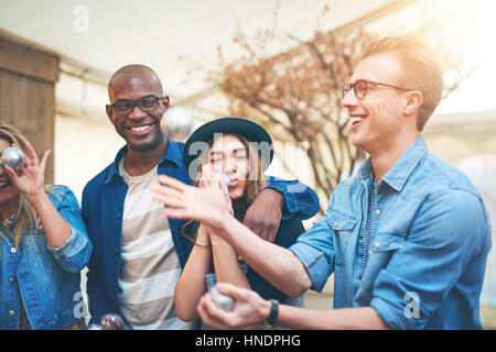 Giovane uomo sorridente e sballottando argento metallico palle di bocce, suoi amici divertendosi e ridendo Foto Stock