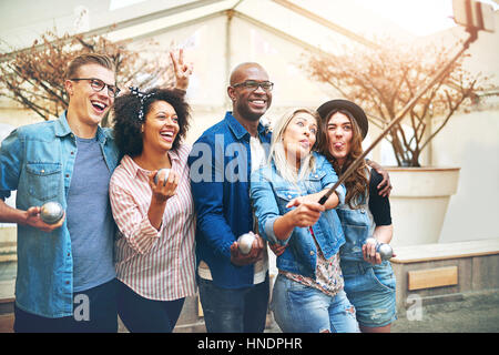 Un gruppo di giovani che pongono a uno smartphone su selfie stick holding petanque sfere metalliche in mani Foto Stock