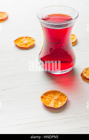 Hibiscus tè in una tazza di vetro su di un tavolo di legno tra i petali di rosa e tè secco crema pasticcera. Copia dello spazio. Foto Stock