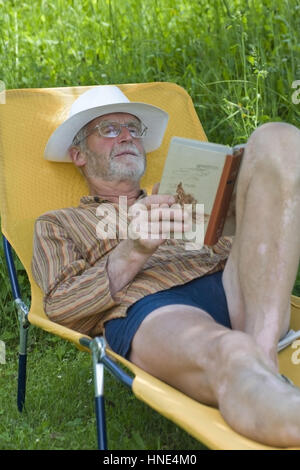 Modello di rilascio, Pensionist, 65+, liegt auf Liegestuhl im Garten und liest ein Buch - titolare di pensione o di rendita che giace su una sedia a sdraio e la lettura di un libro Foto Stock