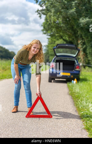 Europeo teenage girl collocando il triangolo di segnalazione sulla strada rurale Foto Stock