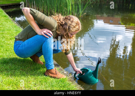 Giovane donna caucasica riempimento orientabile verde con acqua in stagno Foto Stock