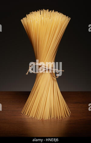 Asciugare gli spaghetti legato con la corda sul legno scuro tabella su sfondo grigio Foto Stock