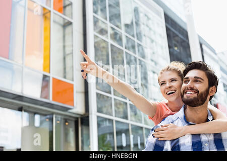 Donna allegra mostrando qualcosa da uomo mentre godendo piggyback Ride in città Foto Stock