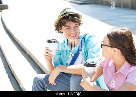Happy amici holding monouso Tazze di caffè seduti sui gradini esterni Foto Stock