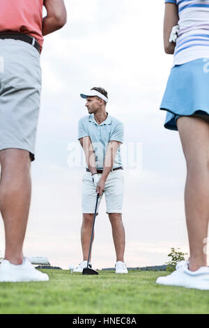 L'uomo giocando a golf contro sky con gli amici in piedi in primo piano Foto Stock