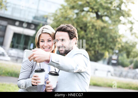 Happy business giovane tenendo selfie tenendo tazze monouso in città Foto Stock