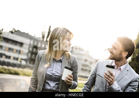 Happy business giovane conversare mentre si tiene tazze monouso in città Foto Stock