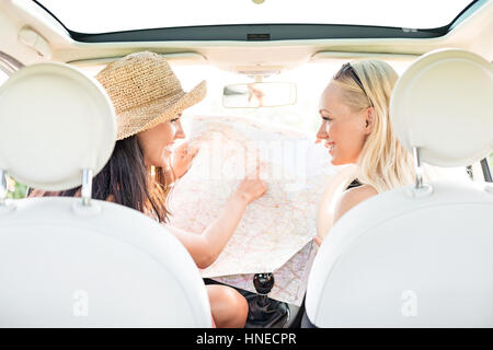 Vista posteriore della femmina felici amici leggere la mappa in auto Foto Stock