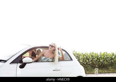 Happy amici di sesso femminile di godere in auto contro il cielo chiaro Foto Stock