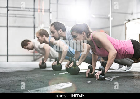 Vista laterale di determinate persone facendo pushups con kettlebells crossfit in palestra Foto Stock