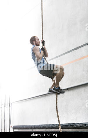 Vista laterale del determinato uomo corda di arrampicata in palestra crossfit Foto Stock