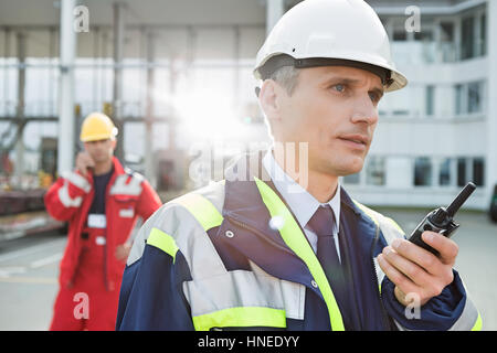 Lavoratore di sesso maschile con un walkie-talkie con il collega in background in cantiere di spedizione Foto Stock