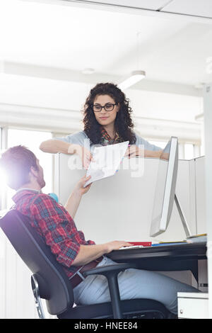Imprenditore consegna documento al collega femmina sulla parete di un cubicolo Foto Stock