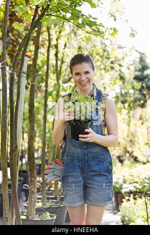 Ritratto di donna felice azienda pianta in vaso in giardino Foto Stock