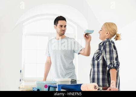 Giocoso uomo mettendo la vernice sulla donna di naso nella nuova casa Foto Stock