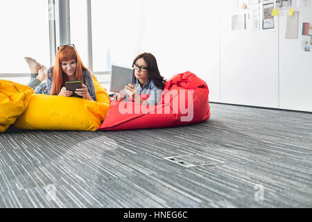 Imprenditrici utilizzando compresse digitale mentre vi rilassate sulle sedie beanbag nel creative office Foto Stock