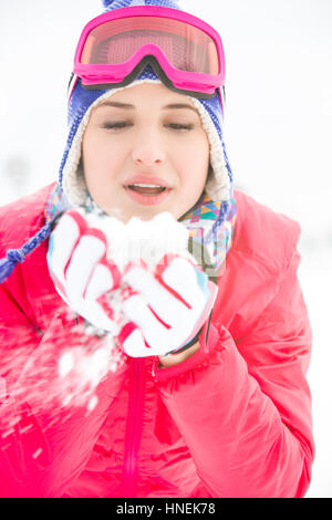 Giovane donna indossa cappotto invernale lavori di soffiaggio della neve all'aperto Foto Stock