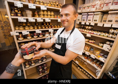 Venditore dando un vasetto di marmellata a femmina cliente nel negozio di alimentari Foto Stock