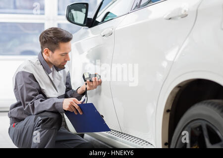 Riparazione maschio lavoratore esaminando la vernice dell'auto con Attrezzature per officina di riparazione Foto Stock