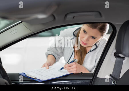 Femmina tecnico di manutenzione con appunti esame auto di interni in officina Foto Stock