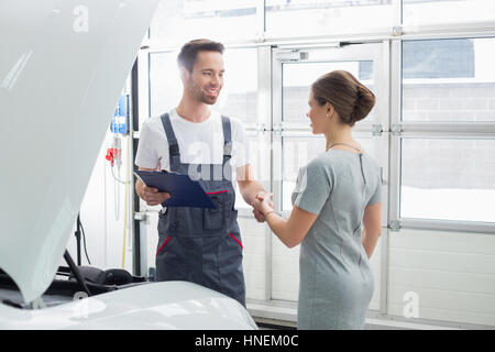 Sorridente tecnico manutenzione stringono le mani con i clienti di sesso femminile in riparazione auto shop Foto Stock