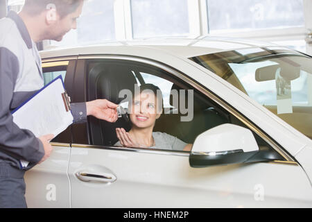 Donna sorridente il cliente riceve chiave auto da meccanico in officina Foto Stock
