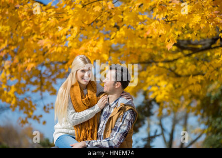 Ritratto di donna felice seduta sull uomo di giro nel parco durante l'autunno Foto Stock