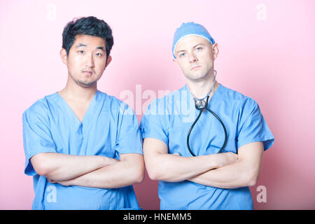 Ritratto di due chirurghi maschio in piedi con le braccia incrociate su sfondo rosa Foto Stock