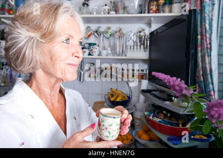 Riflessivo senior donna che guarda lontano tenendo tazza da caffè in cucina Foto Stock