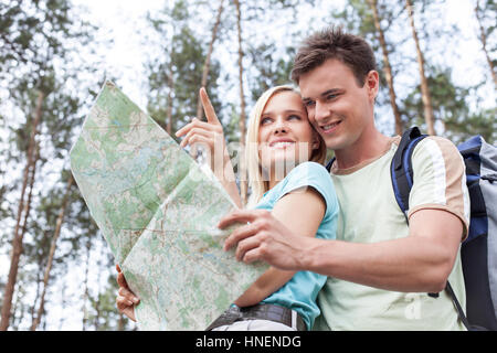 Felice giovani escursionismo giovane azienda mappa con donna rivolto lontano nella foresta Foto Stock